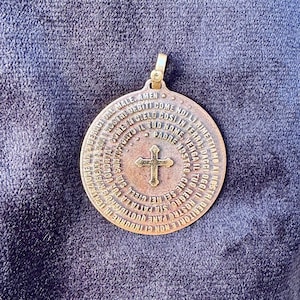 Könnte beinhalten: Ein goldfarbener Anhänger mit einem runden Design, das ein Kreuz und ein Gebet in italienischer Sprache zeigt. Der Anhänger ist aus Metall und hat eine strukturierte Oberfläche.