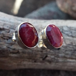 Könnte beinhalten: Ein Paar silberne Ohrstecker mit ovalen roten Rubin-Edelsteinen.
