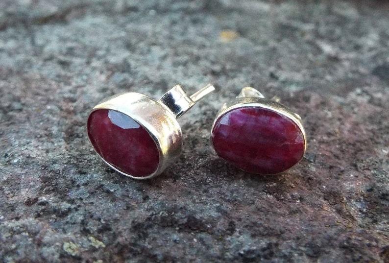 Peut inclure: Une paire de boucles d'oreilles en argent avec des pierres pr&eacute;cieuses en rubis rouge. Les boucles d'oreilles sont de forme ovale et ont une finition lisse et polie.