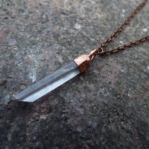 Könnte beinhalten: Ein Anhänger aus klarem Quarzkristall an einer kupfernen Kettenkette. Der Kristall ist facettiert und hat oben eine kupferne Kappe.