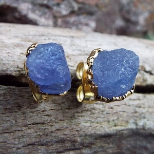 Könnte beinhalten: Ein Paar goldene Ohrringe mit blauen Edelstein-Akzenten. Die Edelsteine sind roh und haben eine natürliche, unregelmäßige Form.