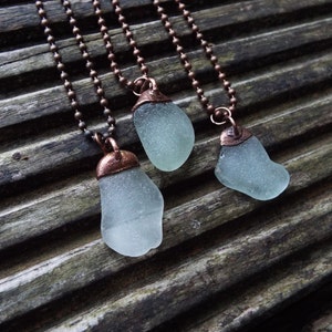 Puede incluir: Tres collares con cadenas de cobre y colgantes de vidrio de mar. El vidrio de mar es de color azul verdoso claro y el cobre es de color marr&oacute;n c&aacute;lido.