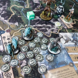 Op de afbeelding: Een bordspel met een groene kaart, dobbelstenen en miniatuurfiguren. De figuren zijn wolven, een ridder en een wezen met een grote bijl. Er zijn ook verschillende tokens met nummers erop.