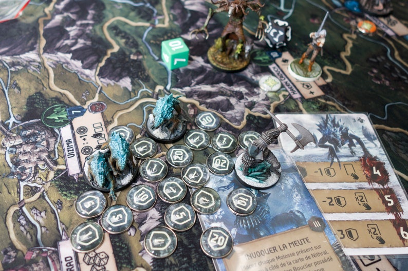 Op de afbeelding: Een bordspel met een groene kaart, dobbelstenen en miniatuurfiguren. De figuren zijn wolven, een ridder en een wezen met een grote bijl. Er zijn ook verschillende tokens met nummers erop.