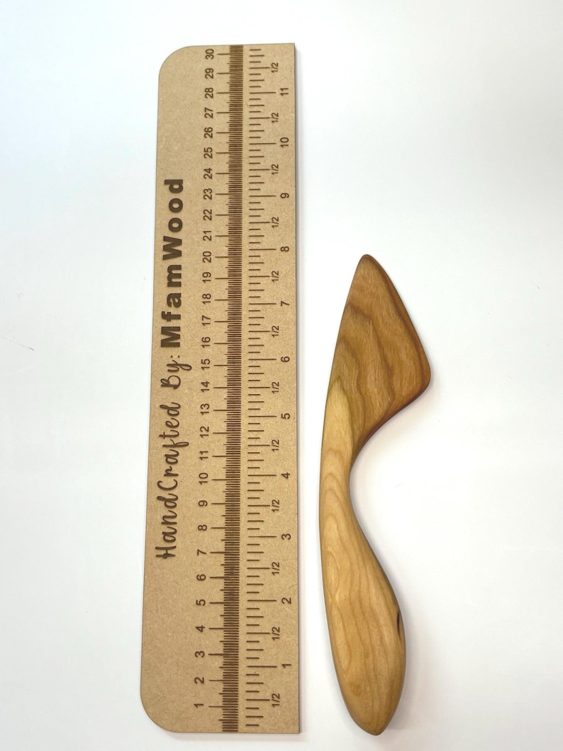 Puede incluir: Un esparcidor de madera de color marr&oacute;n claro con un mango curvo y una hoja plana, colocado junto a una regla de madera que mide 30 cm de largo y presenta el texto HandCrafted By: MfamWood impreso en el lateral.