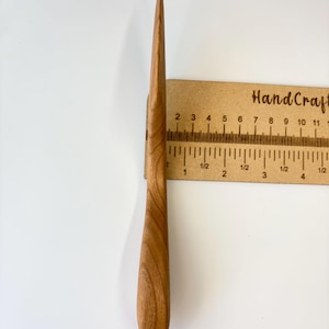 Puede incluir: Un abrecartas de madera de color marr&oacute;n claro con una hoja lisa y afilada y un mango redondeado. La herramienta est&aacute; colocada verticalmente contra una regla, mostrando una longitud total de aproximadamente 11,5 cm desde la punta hasta la base.