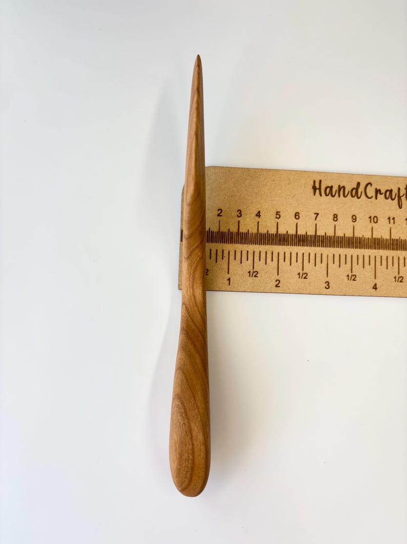 Puede incluir: Un abrecartas de madera de color marr&oacute;n claro con una hoja lisa y afilada y un mango redondeado. La herramienta est&aacute; colocada verticalmente contra una regla, mostrando una longitud total de aproximadamente 11,5 cm desde la punta hasta la base.