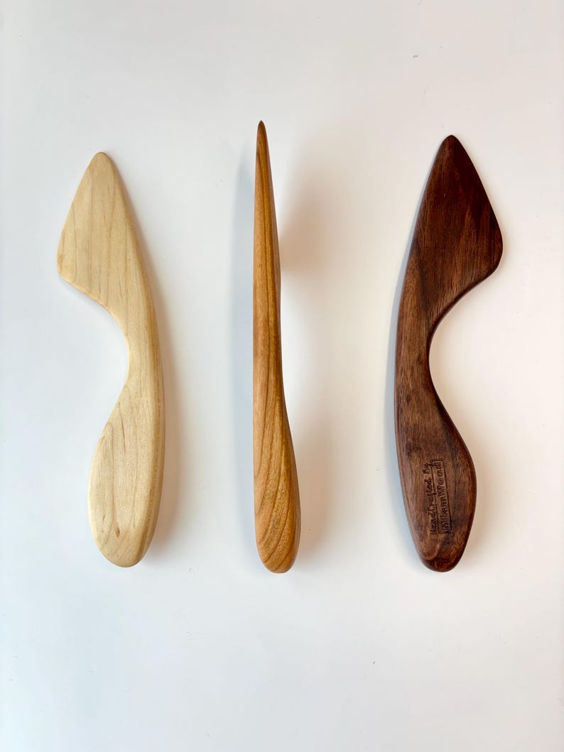 Puede incluir: Tres herramientas de madera con formas suaves y curvas. La herramienta de la izquierda es de color beige claro, la central es una pieza delgada de color marr&oacute;n medio y la de la derecha es marr&oacute;n oscuro con un sello Hand Crafted by Seven Mile Wood.
