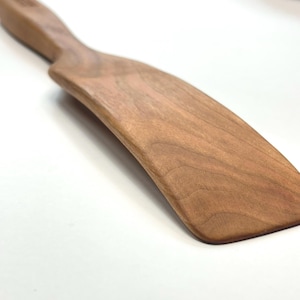 Puede incluir: Una taza de cer&aacute;mica blanca con asa negra y el texto "But First, Coffee" en negrita negra. La taza se encuentra sobre un fondo borroso, sugiriendo un ambiente acogedor.