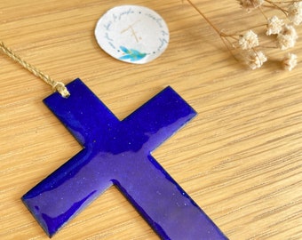 Könnte beinhalten: Ein blaues Kreuz mit glitzerndem Finish, das an einer Bindfadenkordel hängt. Das Kreuz liegt auf einer Holzoberfläche.