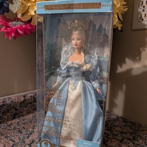 Puede incluir: Una muñeca Barbie titulada Princess of the Danish Court en su empaque original. La muñeca tiene cabello rubio, una corona dorada y viste un vestido azul claro con un cuello de encaje blanco y un panel frontal con un patrón dorado.