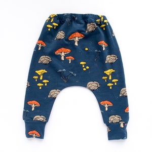 May include: Dark blue baby pants with a whimsical mushroom pattern. The design features various mushroom illustrations in shades of red, yellow, and beige. The pants have a comfortable, elastic waistband and cuffs.