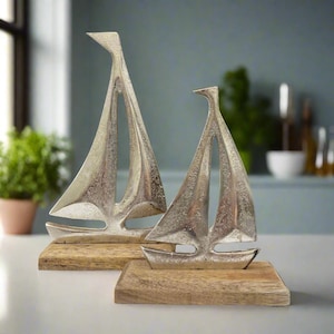 May include: Two silver sailboat sculptures on wooden bases. The sailboats are abstract and modern in design. The larger sailboat is in the background and the smaller sailboat is in the foreground.
