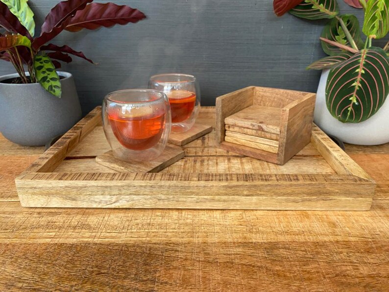 May include: A wooden tray with a natural finish, featuring two glass cups of tea and a set of wooden coasters. The tray is made of solid wood and has a rustic look.