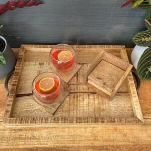May include: A wooden serving tray with two glasses of red liquid and lemon slices. The tray has a natural wood finish and is decorated with a distressed look. There are also two wooden coasters on the tray.