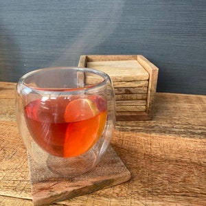 May include: A glass of red tea with a lemon slice in it, sitting on a wooden coaster. The tea is steaming and there is a stack of wooden coasters in the background.