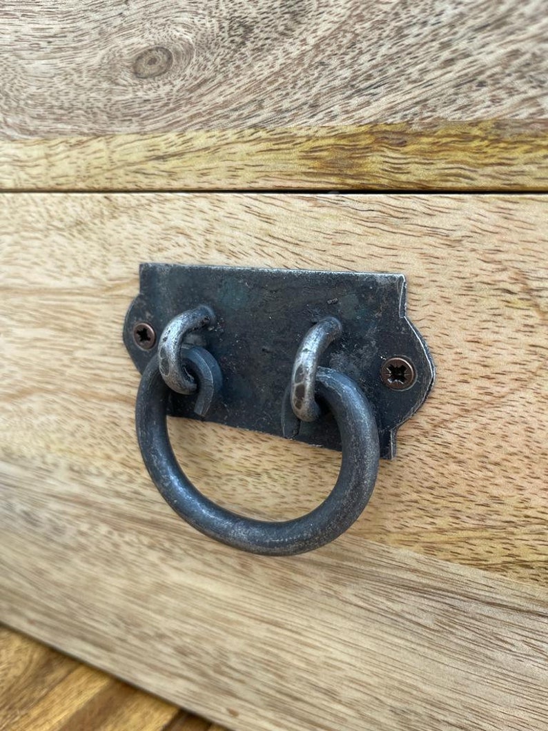 May include: Close-up of a wooden surface with a metal drawer pull. The pull is a dark, aged metal with a ring handle. The wood has a light, natural finish with visible grain.