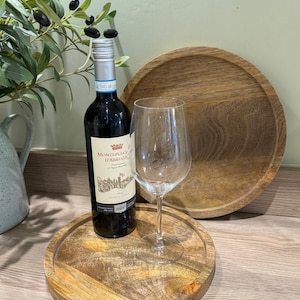 May include: Two round wooden serving trays with a wine bottle and wine glass on top of the smaller tray. The bottle is a dark red wine with a label that says "Montepulciano d'Abruzzo".