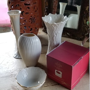 May include: A set of four white Lenox fine china vases and a small bowl with a gold rim. The vases are in a variety of shapes and sizes, and the bowl is round. The items are arranged on a white table with a distressed finish. The box in the image is red and has the Lenox logo and the words "Spode Fine China" printed on it.