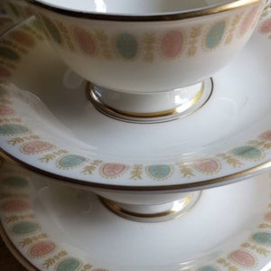 May include: A set of two white teacups and saucers with a gold trim and a delicate floral pattern in shades of pink, blue, and green.