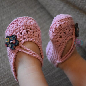 May include: A pair of pink crocheted baby shoes with a flower embellishment on one shoe.