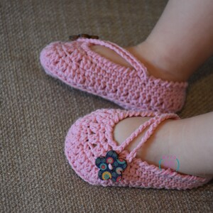 May include: A pair of pink crocheted baby shoes with a flower button on each shoe.