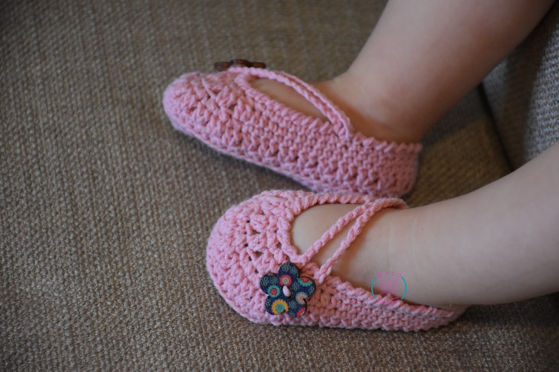 May include: A pair of pink crocheted baby shoes with a flower button on each shoe.