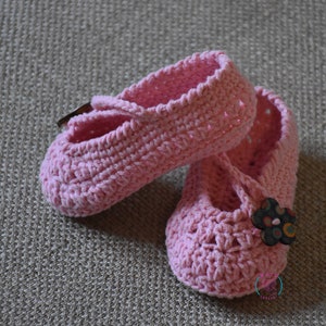 May include: A pair of pink crocheted baby shoes with a flower embellishment on one shoe.