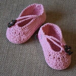 May include: A pair of pink crocheted baby shoes with a flower button on each shoe.