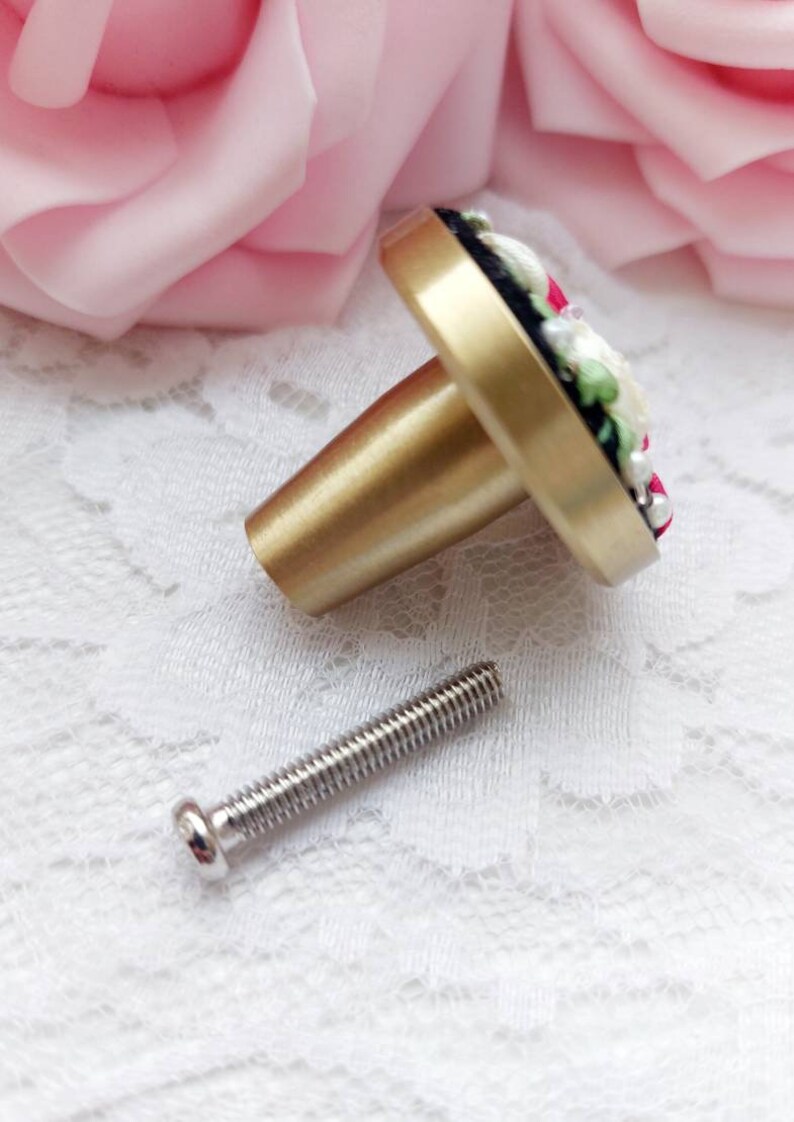 Peut inclure: Un bouton de porte en or avec un motif floral compos&eacute; de fleurs blanches et roses, de feuilles vertes et d'accents noirs. Le bouton est livr&eacute; avec une vis argent&eacute;e.