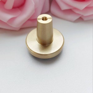 Peut inclure: Un bouton en m&eacute;tal dor&eacute; avec une base ronde et un dessus cylindrique. Le bouton a un trou filet&eacute; en haut pour le fixer &agrave; un tiroir ou une armoire.