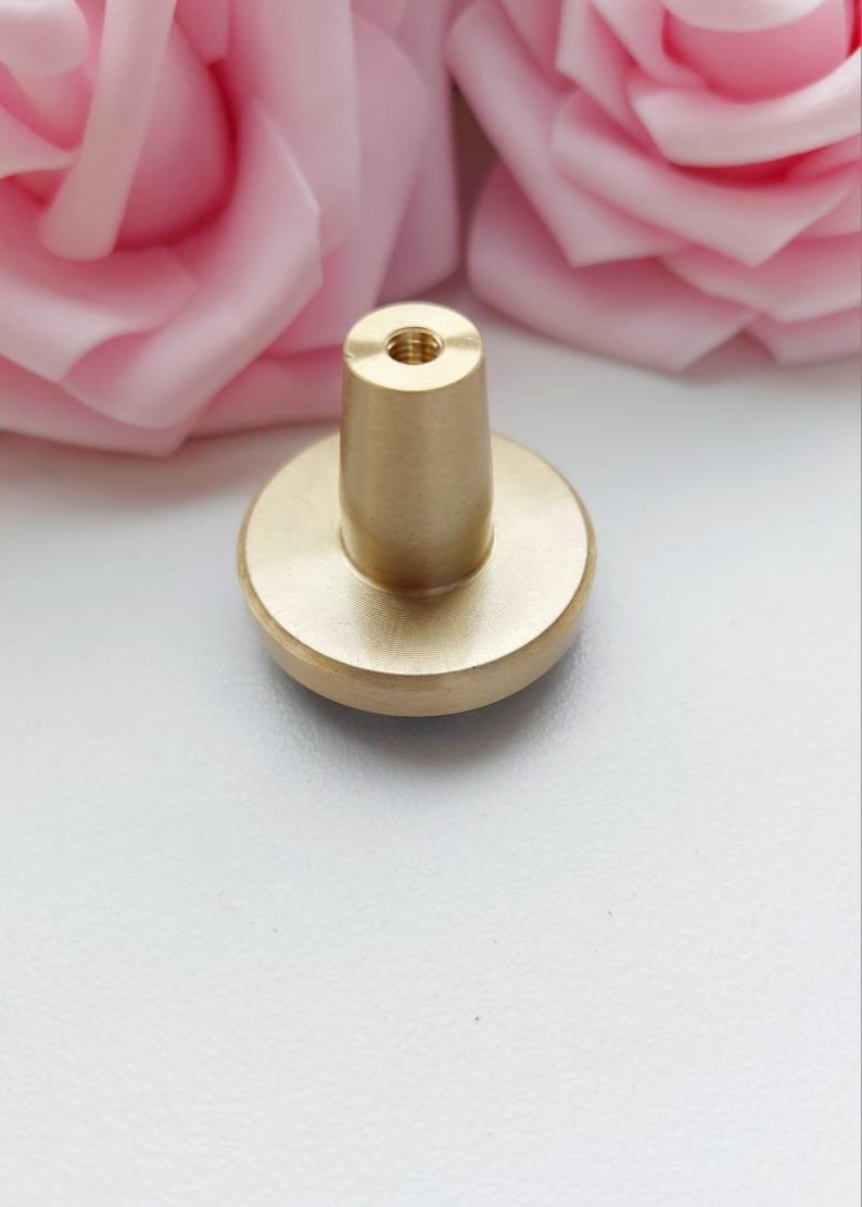 Peut inclure: Un bouton en m&eacute;tal dor&eacute; avec une base ronde et un dessus cylindrique. Le bouton a un trou filet&eacute; en haut pour le fixer &agrave; un tiroir ou une armoire.