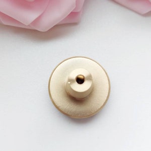 Peut inclure: Bouton en m&eacute;tal dor&eacute; de forme circulaire avec un petit trou au centre. Le bouton a un bord l&eacute;g&egrave;rement sur&eacute;lev&eacute; et une surface textur&eacute;e.