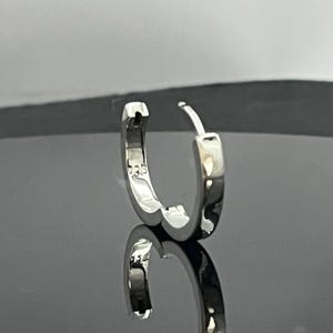 May include: A polished silver hoop earring with a hinged closure mechanism. The inner surface of the hoop is clearly stamped with the number 925, indicating sterling silver composition. The earring has a smooth, reflective metallic finish.