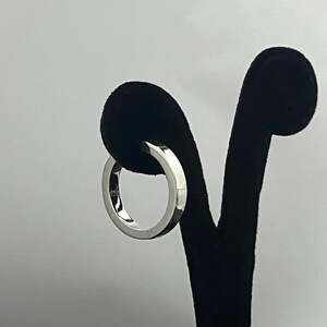 May include: A polished silver-colored ring with a smooth, flat band design. The interior of the band features a small, clear engraving that reads 925, indicating the metal composition. The ring has a reflective, metallic finish throughout.