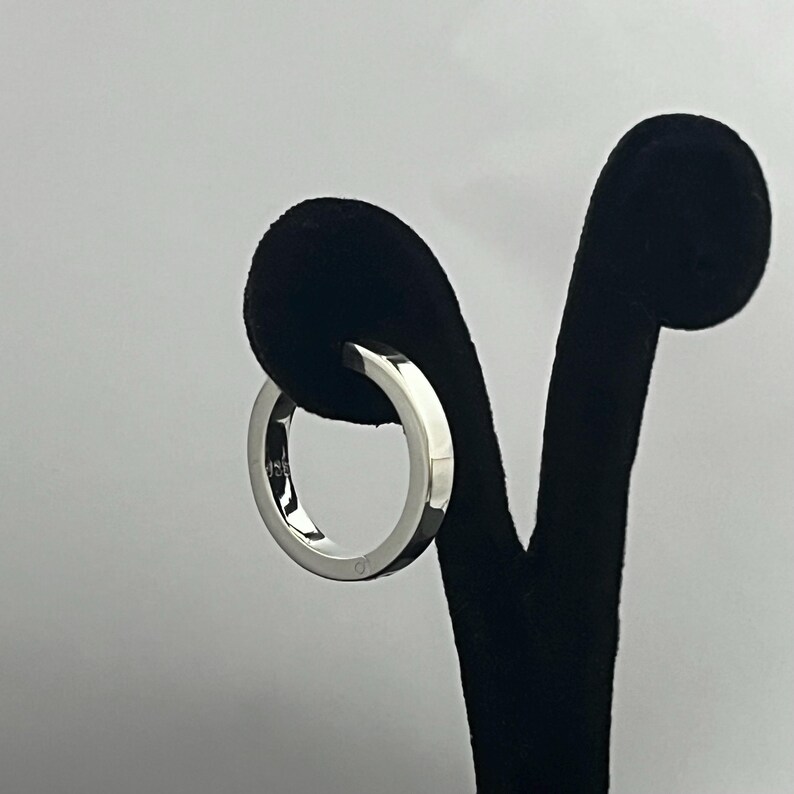 May include: A polished silver-colored ring with a smooth, flat band design. The interior of the band features a small, clear engraving that reads 925, indicating the metal composition. The ring has a reflective, metallic finish throughout.