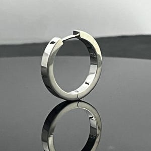 May include: A polished silver-tone hoop earring with a hinged closure mechanism. The metal surface is smooth and reflective, featuring a small 925 hallmark stamp on the inner band, indicating sterling silver composition for this circular jewelry piece.