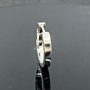 May include: A single silver-toned hoop earring with a polished, reflective surface. The earring features a hinged closure mechanism at the top, showing a smooth, rounded profile and a metallic finish that catches the light, creating a clean look.