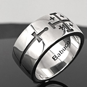 May include: A polished silver-toned ring featuring a wide band with an engraved Jerusalem cross and a sword motif on the outer surface. The interior of the band is clearly engraved with the word Babuco in a clean, dark, sans-serif typeface.