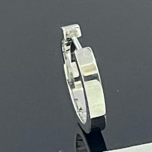 May include: A silver-toned hoop earring with a hinged closure mechanism. The earring features a polished, reflective metallic surface with a rectangular cross-section and a smooth, continuous circular design that curves to form a complete hoop.