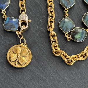 May include: Gold-toned necklaces with labradorite gemstones and a clover charm. The necklaces feature a chunky chain design and a diamond-studded clasp. The labradorite stones have a blue and green iridescent sheen.