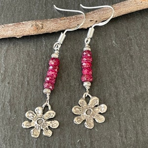 May include: A pair of silver earrings with a dangling flower charm and a strand of red gemstone beads.