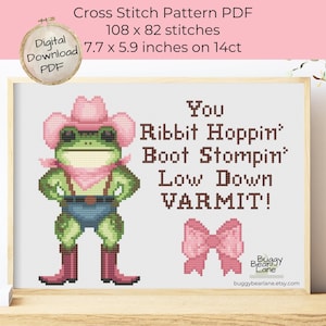 Puede incluir: Patrón de punto de cruz PDF con una rana verde con sombrero y botas de vaquero, con el texto "You Ribbit Hoppin' Boot Stompin' Low Down VARMIT!". El patrón mide 19.5 x 15 cm e incluye un lazo rosa.