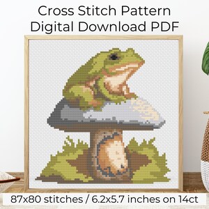 May include: Cross stitch pattern PDF download of a green frog sitting on a mushroom with brown and gray accents. The pattern is 87x80 stitches and measures 6.2x5.7 inches on 14 count Aida cloth.
