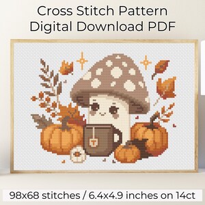 Op de afbeelding: PDF-patroon voor kruissteek met een schattige paddenstoel die een kopje thee vasthoudt, omringd door pompoenen en herfstbladeren. Het patroon is 98x68 steken en meet 16,3x12,4 cm op 14-count Aida-stof.