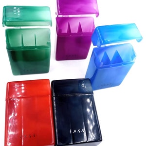 May include: Five plastic cigarette cases in different colors: green, purple, blue, red, and black. Each case has a hinged lid and a compartment for cigarettes. The cases are all labeled with the text "f.e.s.s."