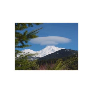 Può includere: Una cima di montagna innevata con una nube lenticolare sopra, incorniciata da pini verdi.