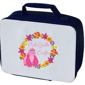 Pode incluir: Uma bolsa de almo&ccedil;o branca com um z&iacute;per e uma al&ccedil;a azul marinho. A bolsa apresenta um gorila rosa usando uma coroa de flores cercada por uma guirlanda de flores coloridas. O texto "Pink Gorilla Crafts" est&aacute; impresso na bolsa.