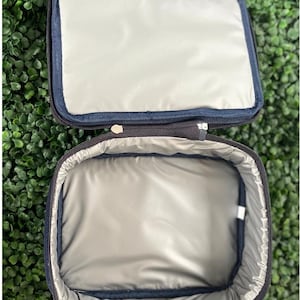Pode incluir: Uma bolsa de almo&ccedil;o isolada preta com fecho de correr. A bolsa est&aacute; aberta e o interior &eacute; forrado com um material prateado.