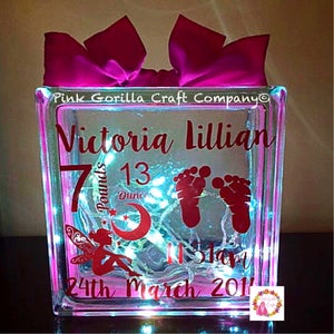 Op de afbeelding: Een heldere glazen blok met een roze strik erop. De blok heeft een fee, een halve maan, sterren en voetafdrukken erop. Er staat ook de tekst "Victoria Lillian", "7 pond 13 ons" en "24 maart 2011" op.